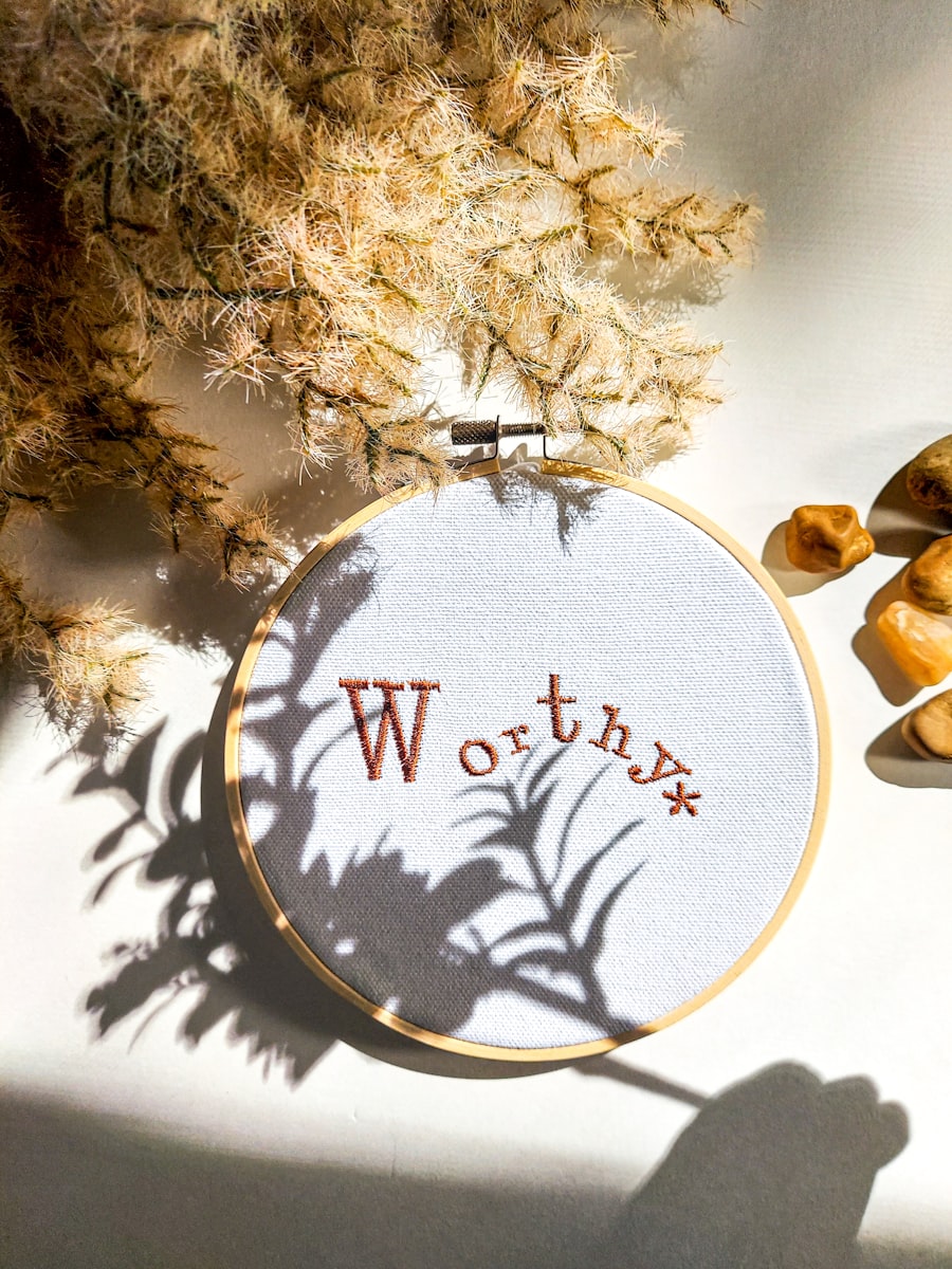 Embroidery hoop with rust serif lettering reading Worthy on white fabric